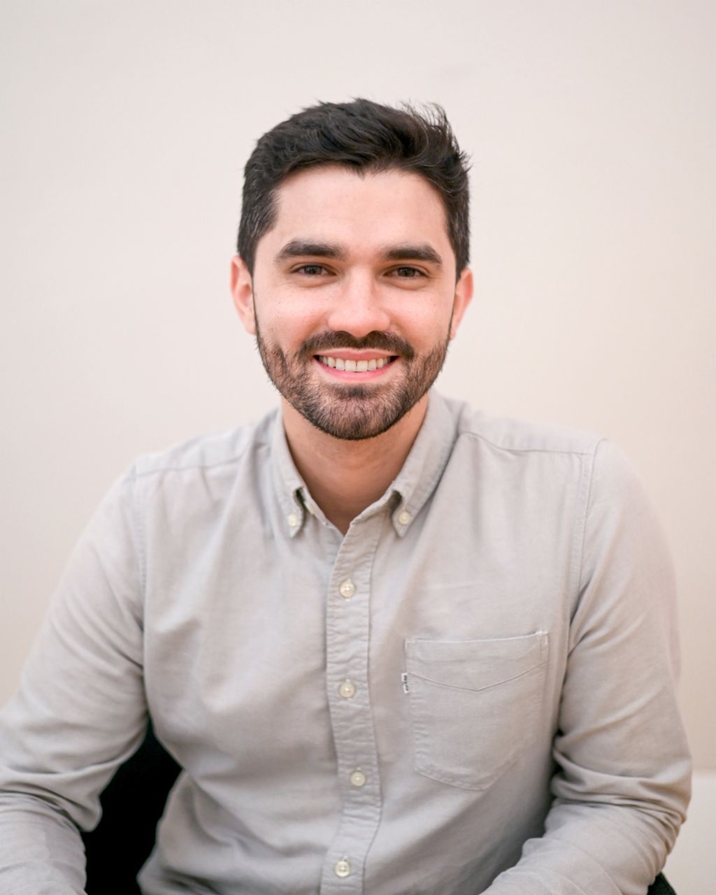 Lucas Antunes sitzt vor einer weißen Wand und lächelt aufrichtig.