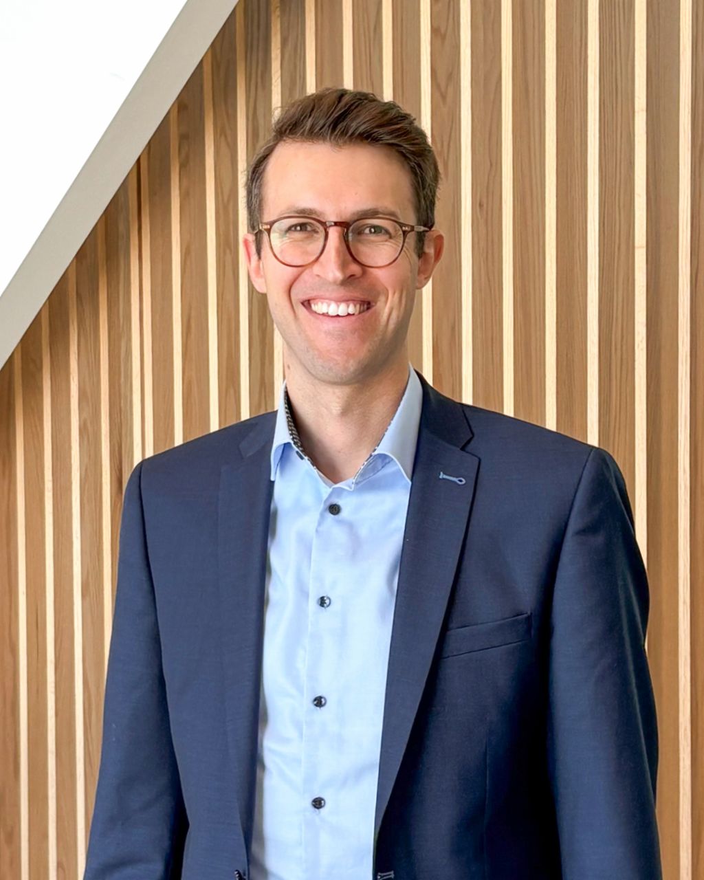 Portrait of Fabio Buschle wearing glasses in front of wooden panels.