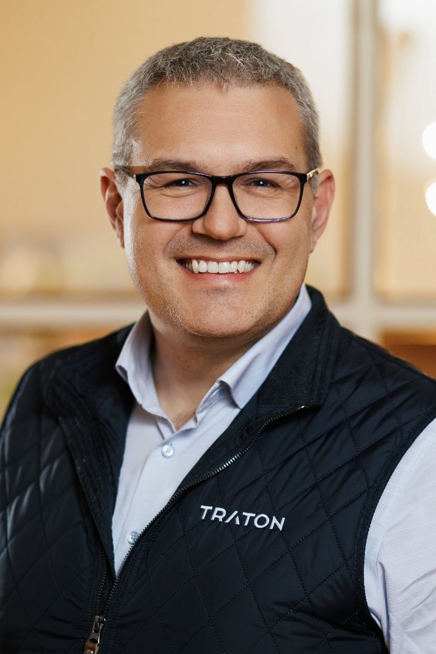 Stefan Riegl, Domain Head for Systems Engineering at TRATON GROUP R&D wearing black glasses, a blue shirt and black vest with the TRATON logo on the right side. 