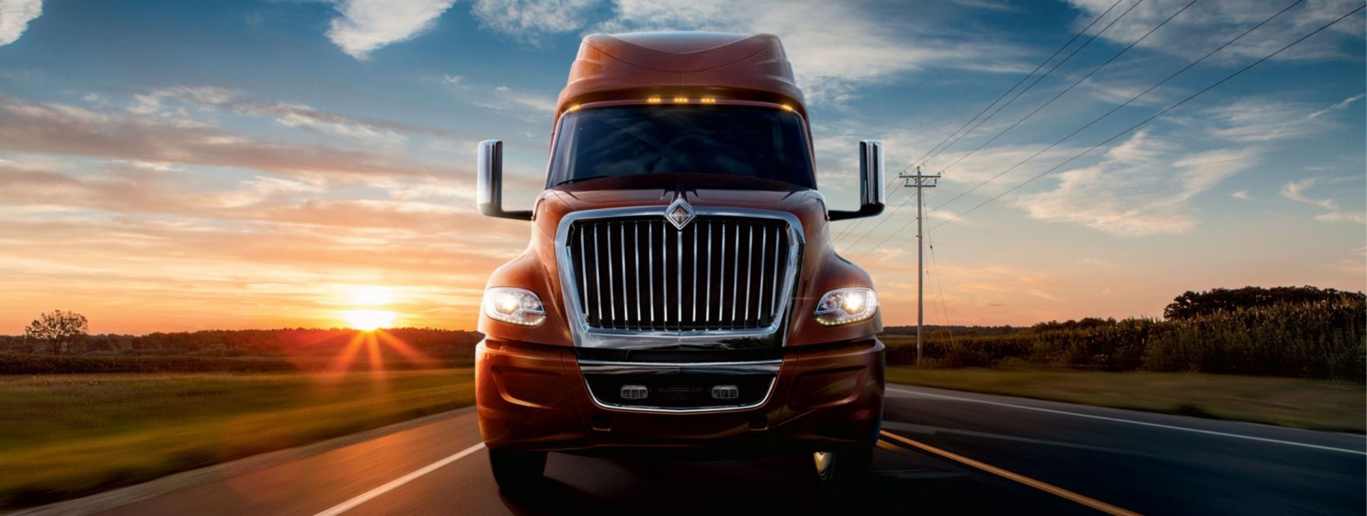 Image of a red NAVISTAR truck on the road in front of a sunrise