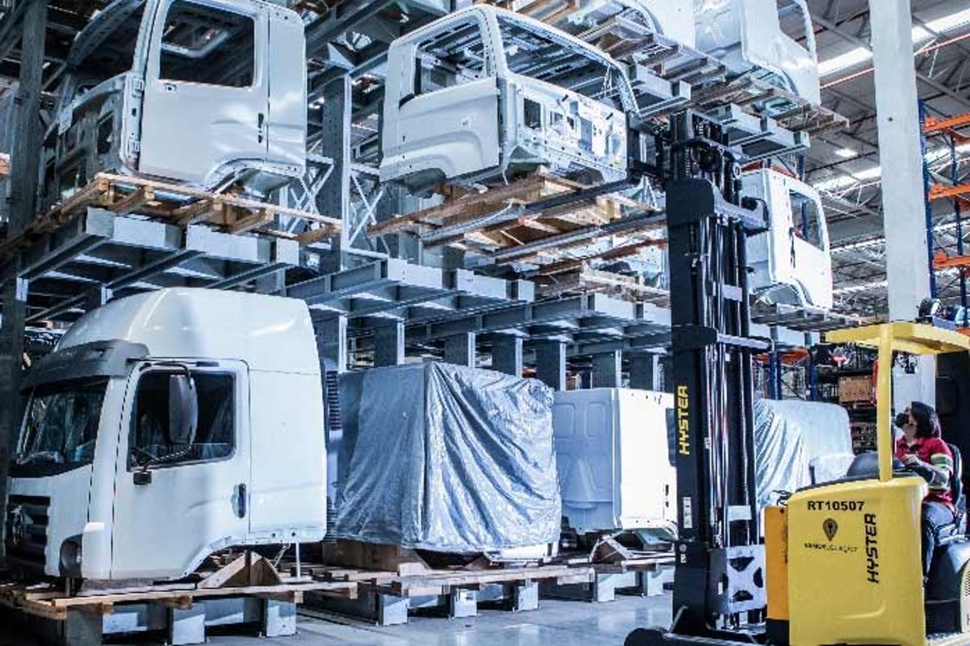 Ein Gabelstapler transportiert Teile von Lkw-Fahrerhäusern in einem großen Industrie-Lager mit gestapelten Kabinen.