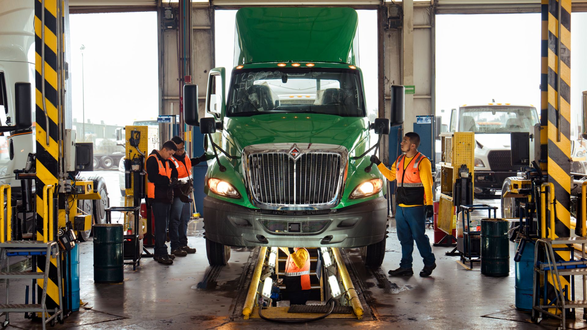 International employees wearing security vests surrounding a green International truck and working underneath it. 