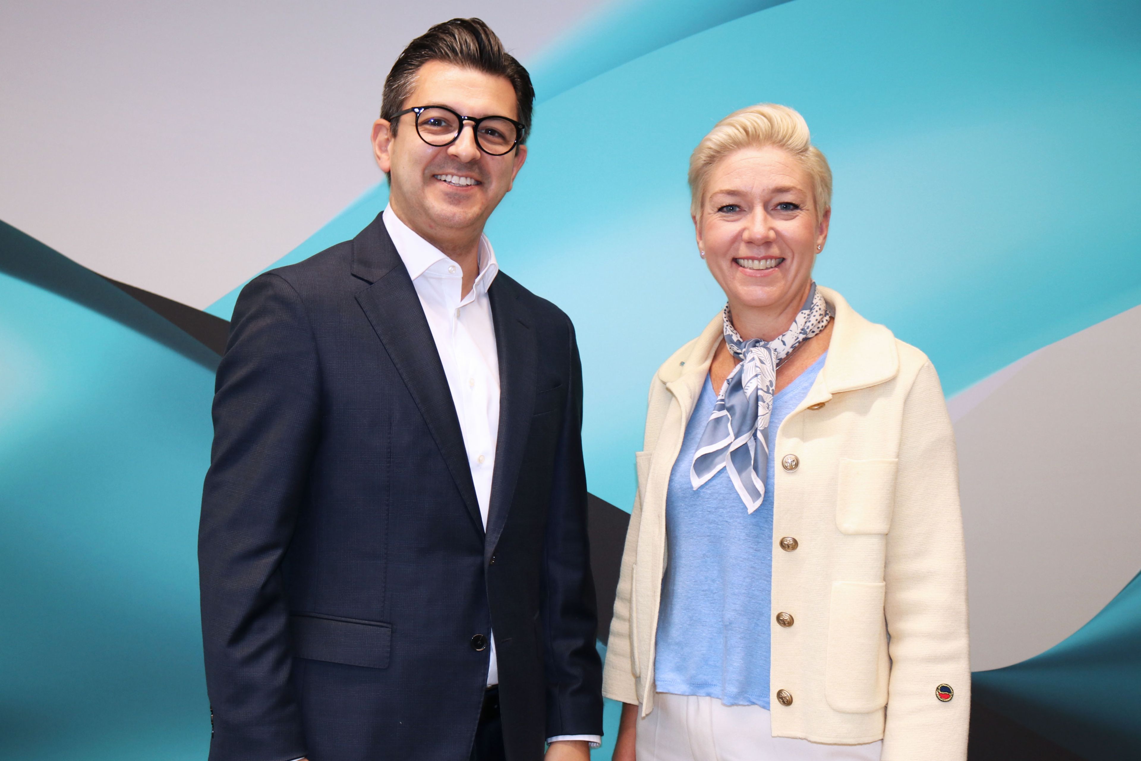 Eine Frau und ein Mann stehen lächelnd vor einer türkisfarbenen Wand.