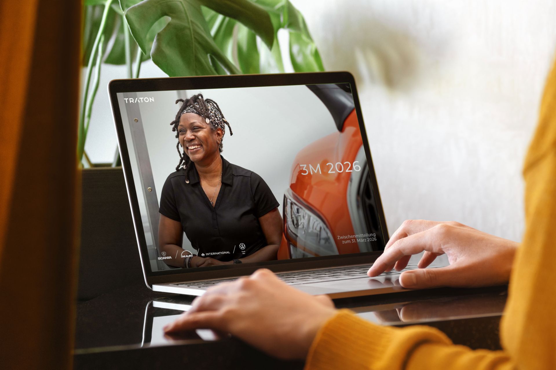 Hände einer Person, die einen Laptop betrachtet. Auf dem Bildschirm wird das Cover des TRATON 3M-Berichts angezeigt.
                 