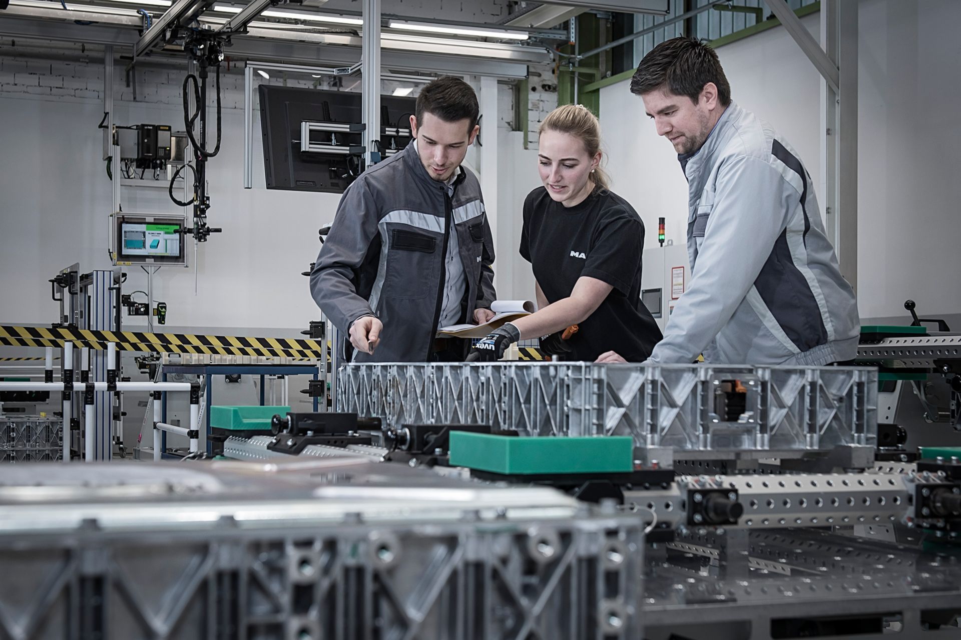 Drei Personen besichtigen eine MAN-Batterieproduktion in Nürnberg.
                 